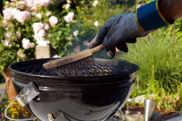 Person reinigt Grillrost mit Bürste